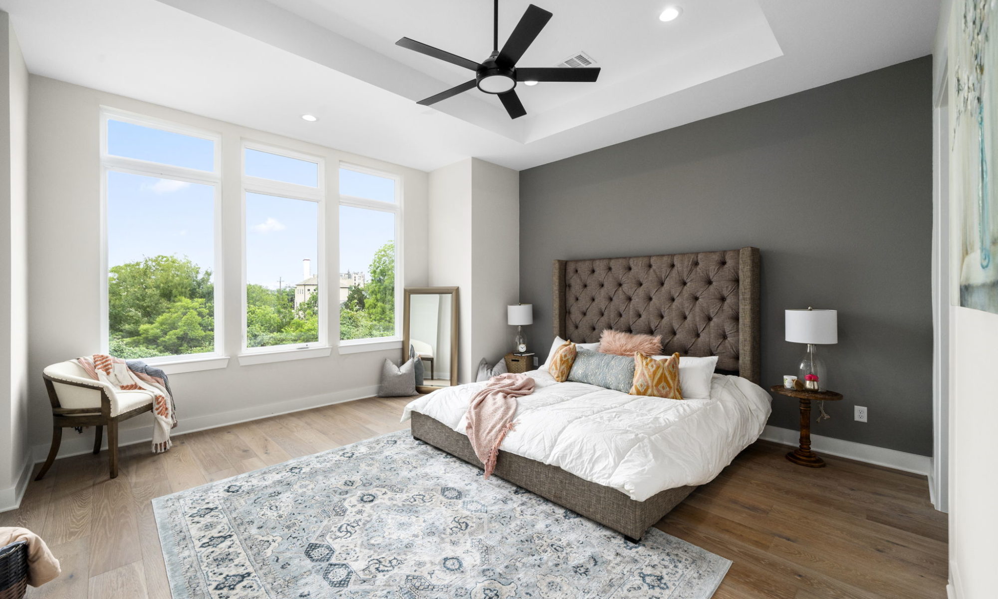 Master bedroom with king size bed and three large windows looking out to trees