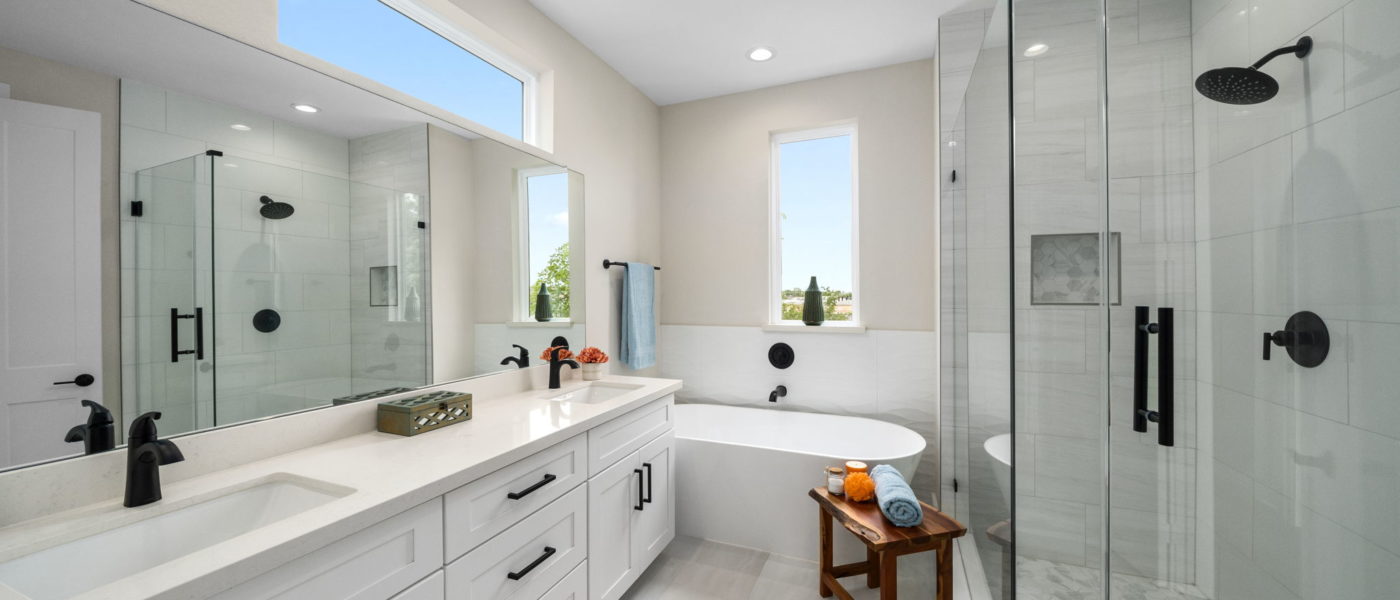 Master bathroom with vanity, freestanding tub, frameless glass shower, transom window and window showing blue sky.
