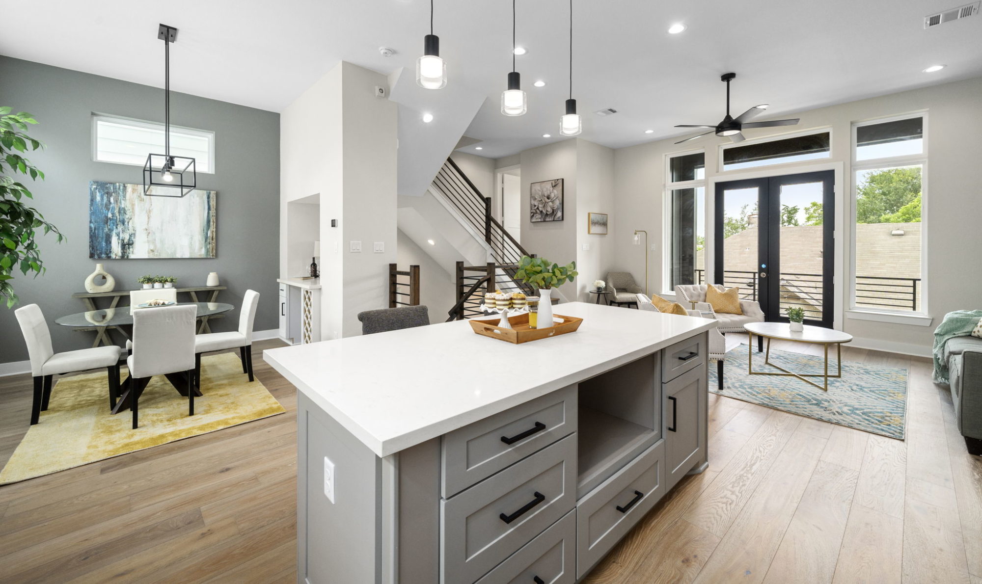 View from kitchen of kitchen island, patio french doors, custom staircase, staged dining room, wine bar, staged living room, and staged living room.